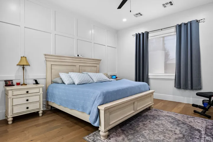 White paneled accent wall, wood-finish flooring, recessed lighting, ceiling fan, and window with white trim