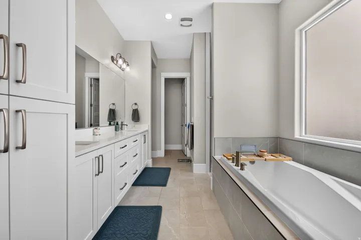 Dual vanity with white cabinetry and integrated sinks, a built-in soaking tub with tiled surround, and a frosted privacy window