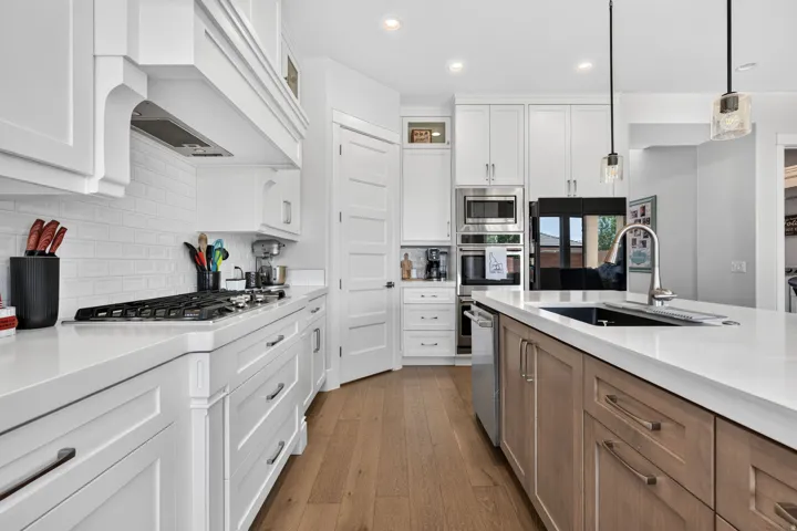 Spacious kitchen featuring white shaker cabinetry, light-toned wood-finish flooring, a kitchen island with sink, subway tile backsplash, and stainless steel appliances