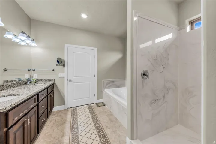 Dual vanity with stone countertop, built-in bathtub, and walk-in shower with patterned wall panels
