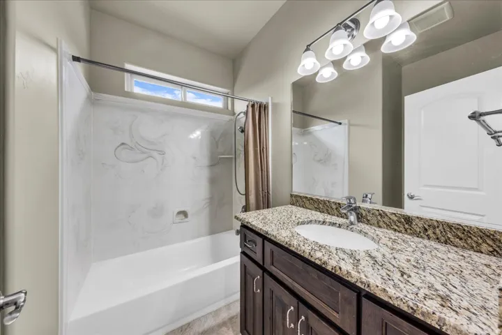 Tub/shower combination with a textured surround, single vanity with a granite countertop, oval undermount sink, and dark wood-finish cabinetry