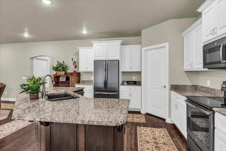 Kitchen featuring a large island with an undermount sink, light-toned countertops, white cabinetry, dark wood-finish flooring, and recessed lighting