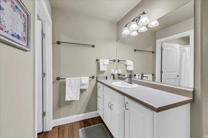 Wood-finish flooring, white vanity with ample storage, integrated sink, and a large wall-mounted mirror