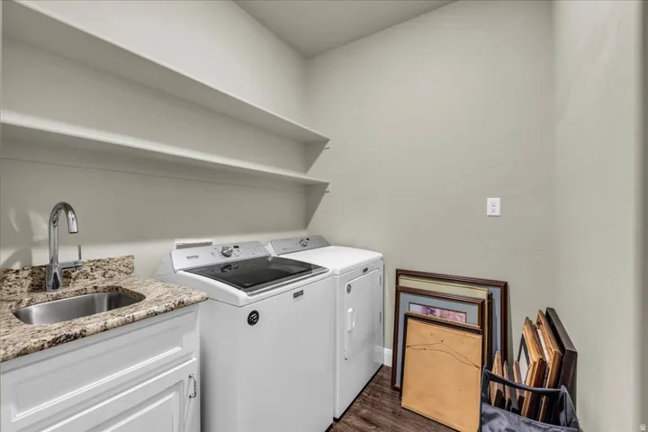 Laundry area featuring a built-in sink, granite-style countertop, white cabinetry, and wood-finish flooring