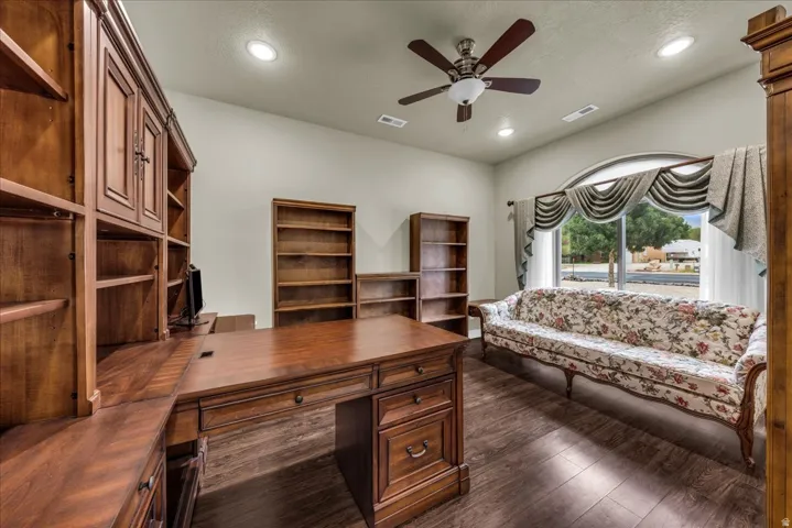 Built-in wood cabinetry, wood-finish flooring, a ceiling fan with integrated lighting, recessed lighting, and a large arched window with decorative window treatments