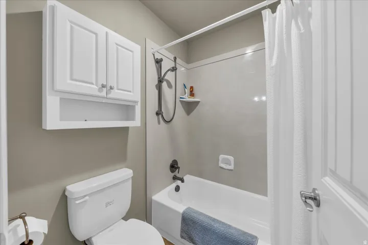 Clean and functional bathroom featuring white cabinetry with ample storage, a white porcelain toilet, and a bathtub/shower combination with gray tile surround and chrome fixtures