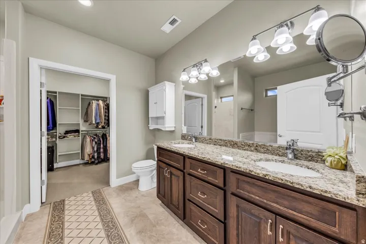 Dual vanity with a stone countertop, individual sinks, and overhead lighting