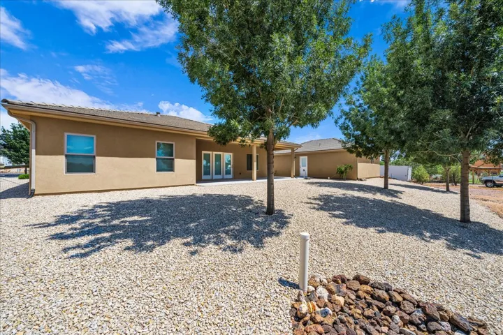 Stucco exterior with multiple windows, a rear patio, and a gravel yard with mature trees