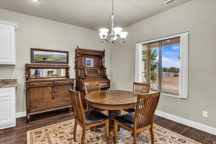 Wood-finish flooring, white cabinetry, granite countertop, and a window with vertical blinds