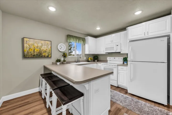 Kitchen featuring white cabinetry, integrated appliances, wood-finish flooring, recessed lighting, and a breakfast bar