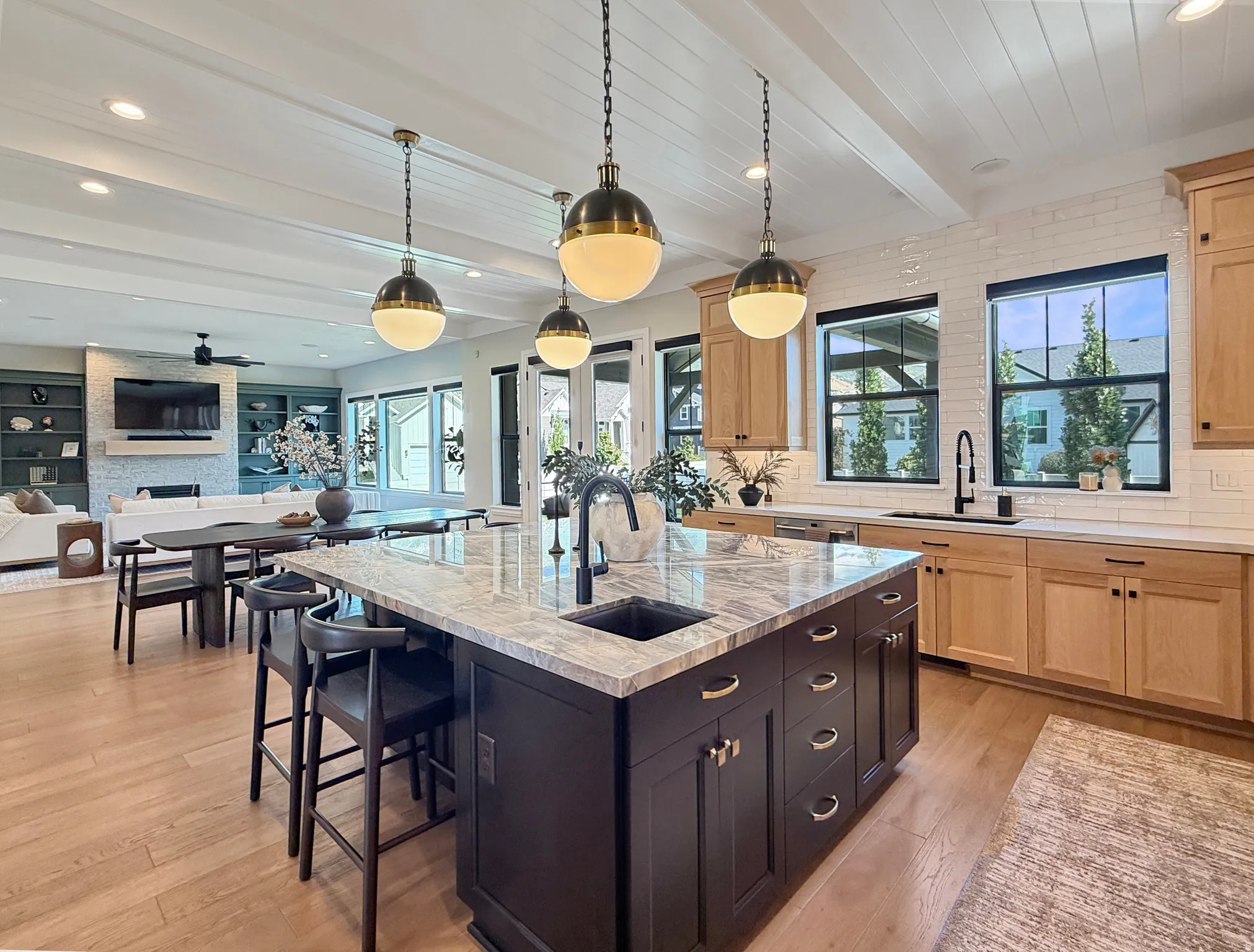 Open-concept kitchen with a large island featuring a built-in sink, pendant lighting, light wood-finish flooring, and white subway tile backsplash