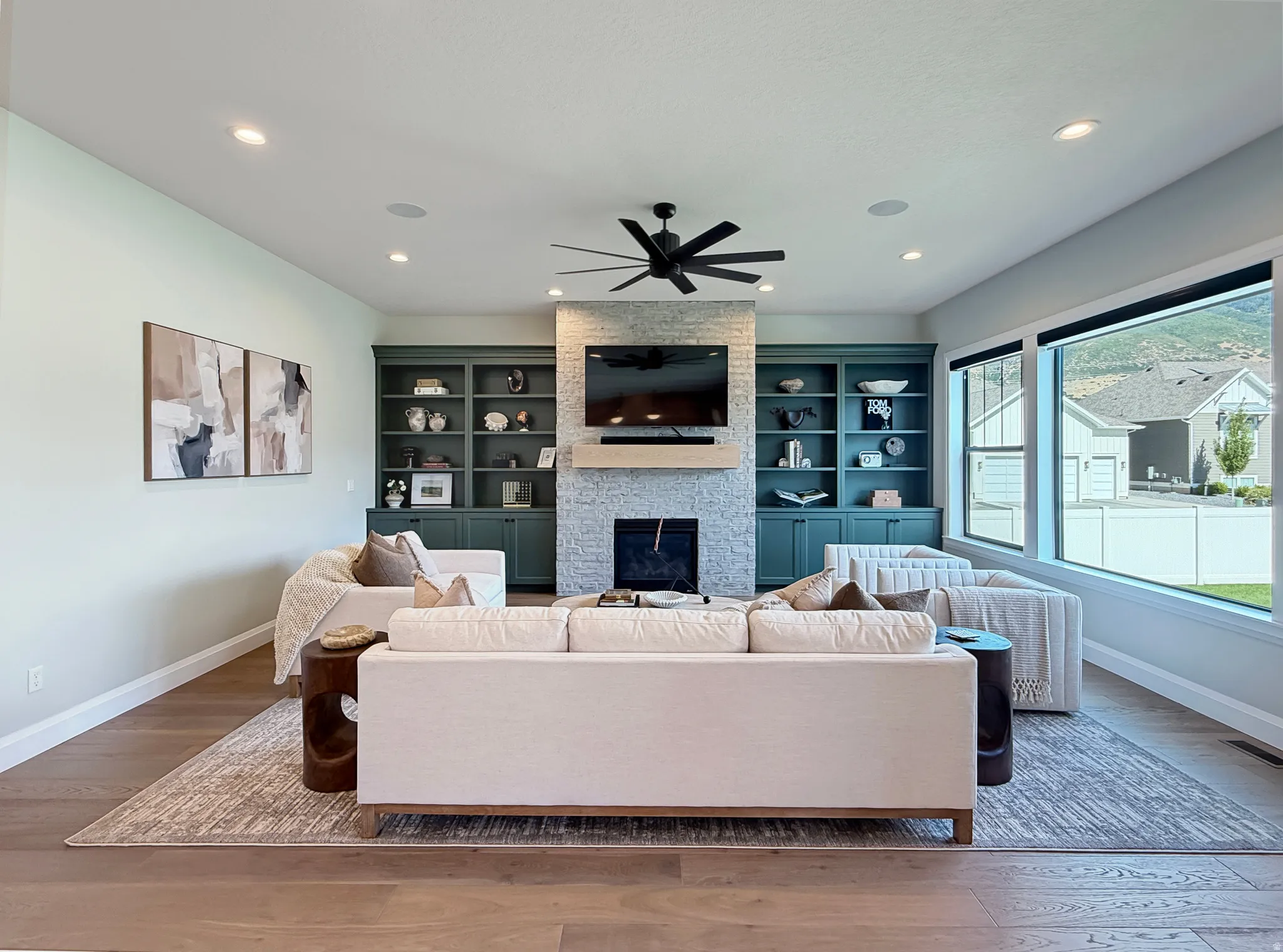 Living area featuring wood-finish flooring, built-in shelving, a stone fireplace, recessed lighting, and large windows