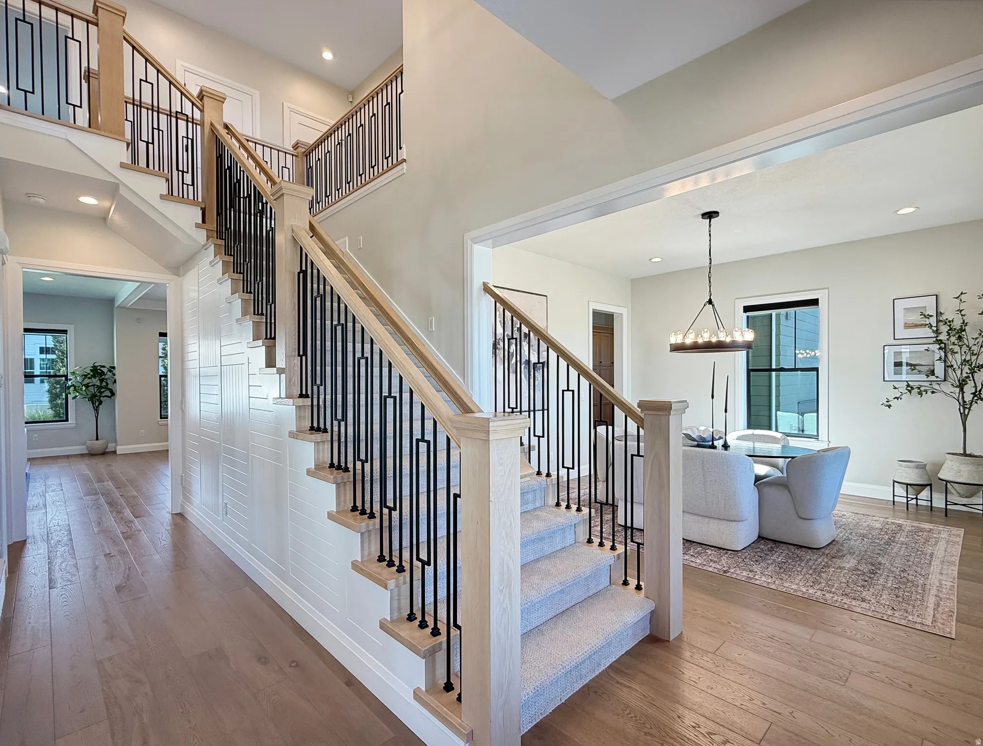 Two-story entryway featuring wood-finish flooring, a carpeted staircase with wood newel posts, and decorative metal balusters