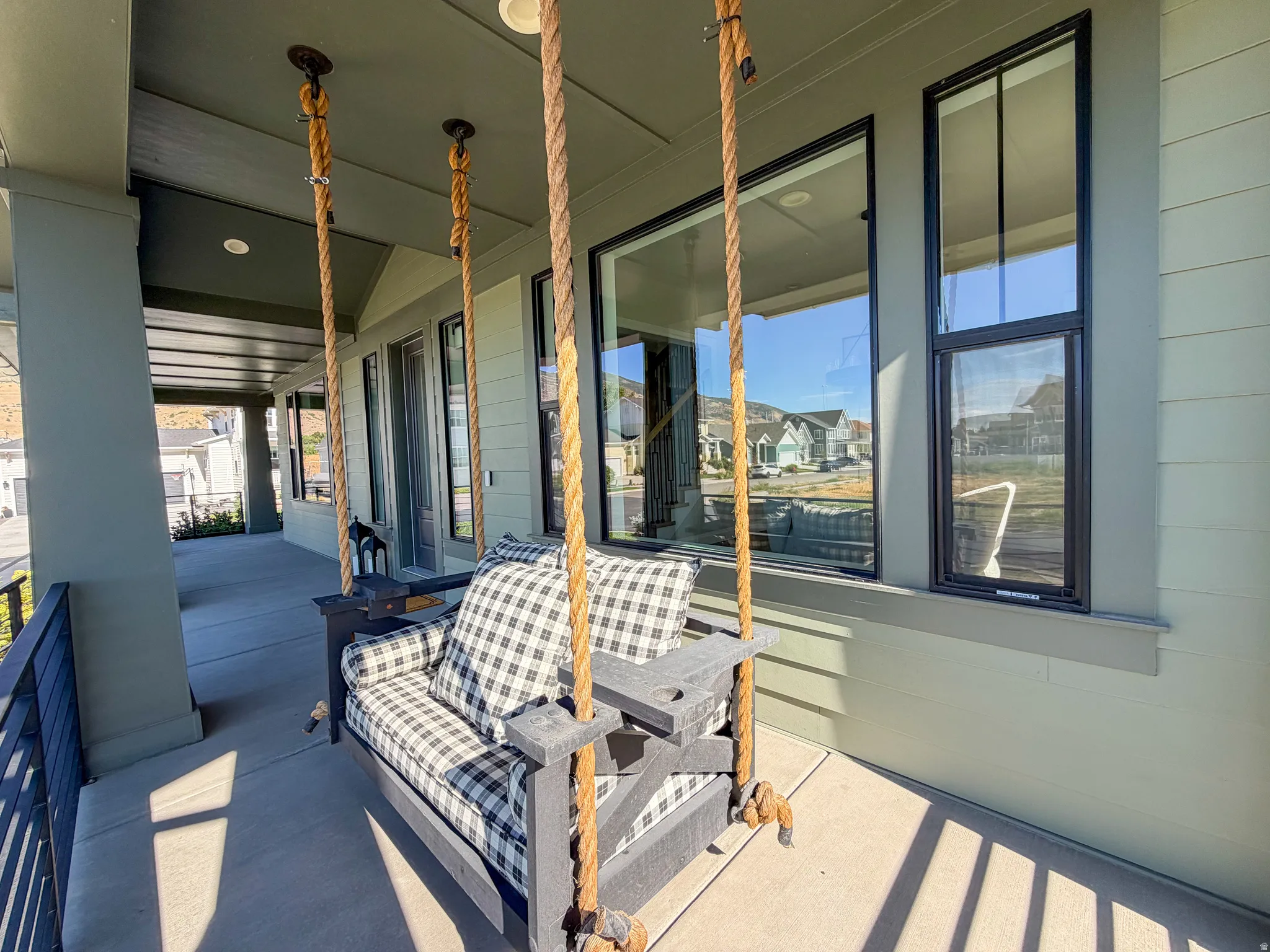 Covered porch with concrete flooring, vertical siding, black-framed windows, and a metal railing