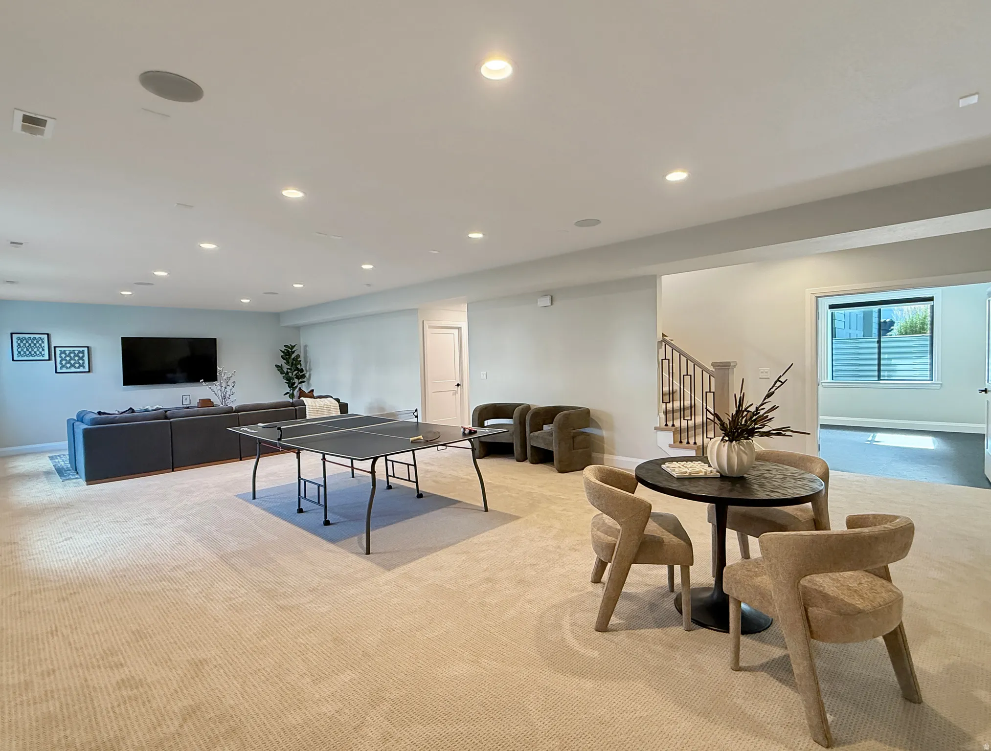 Expansive carpeted living space with recessed lighting, a built-in sound system, and a staircase featuring a decorative metal railing