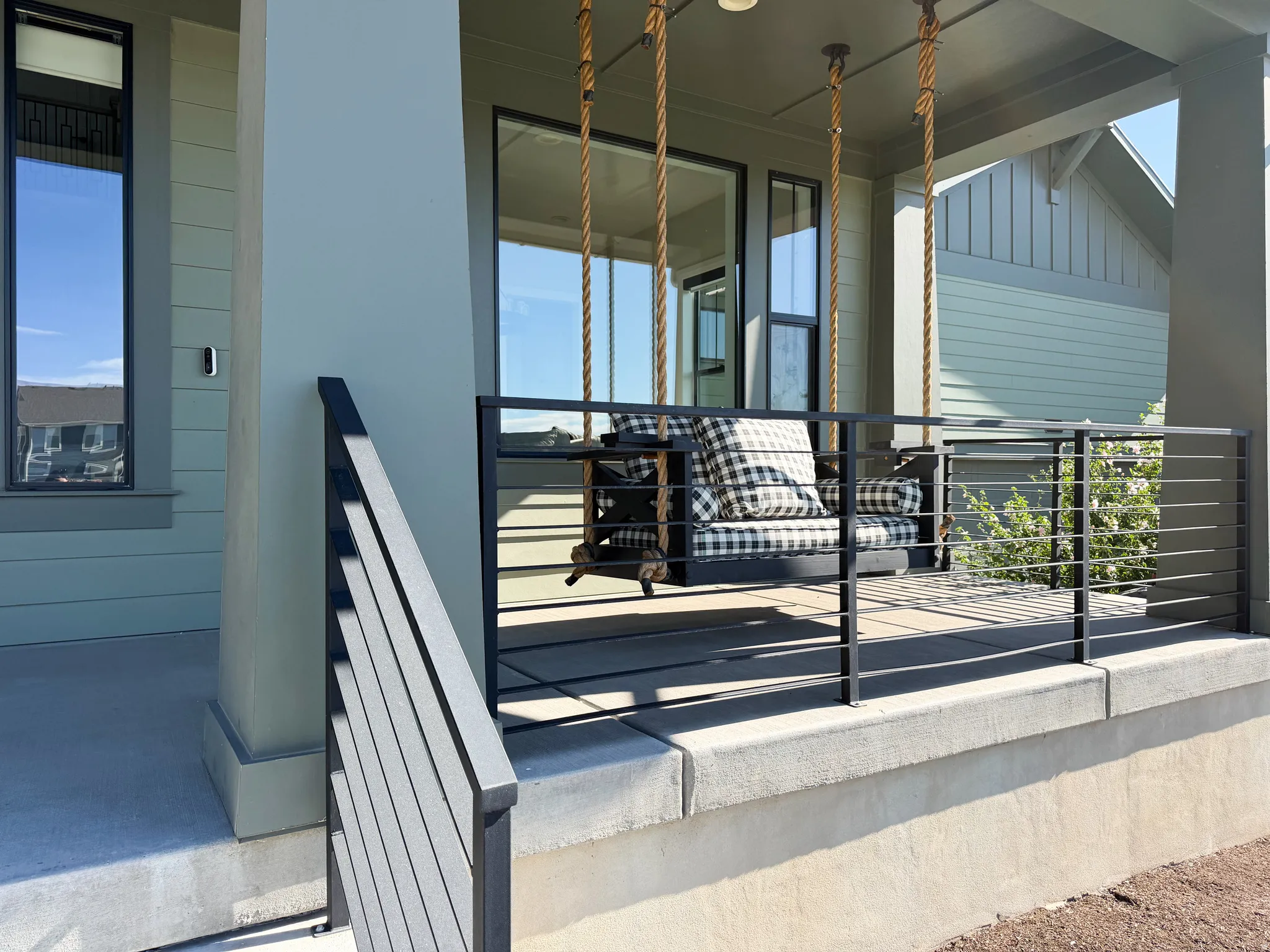 Covered porch with concrete flooring, modern black metal railing, and vertical window