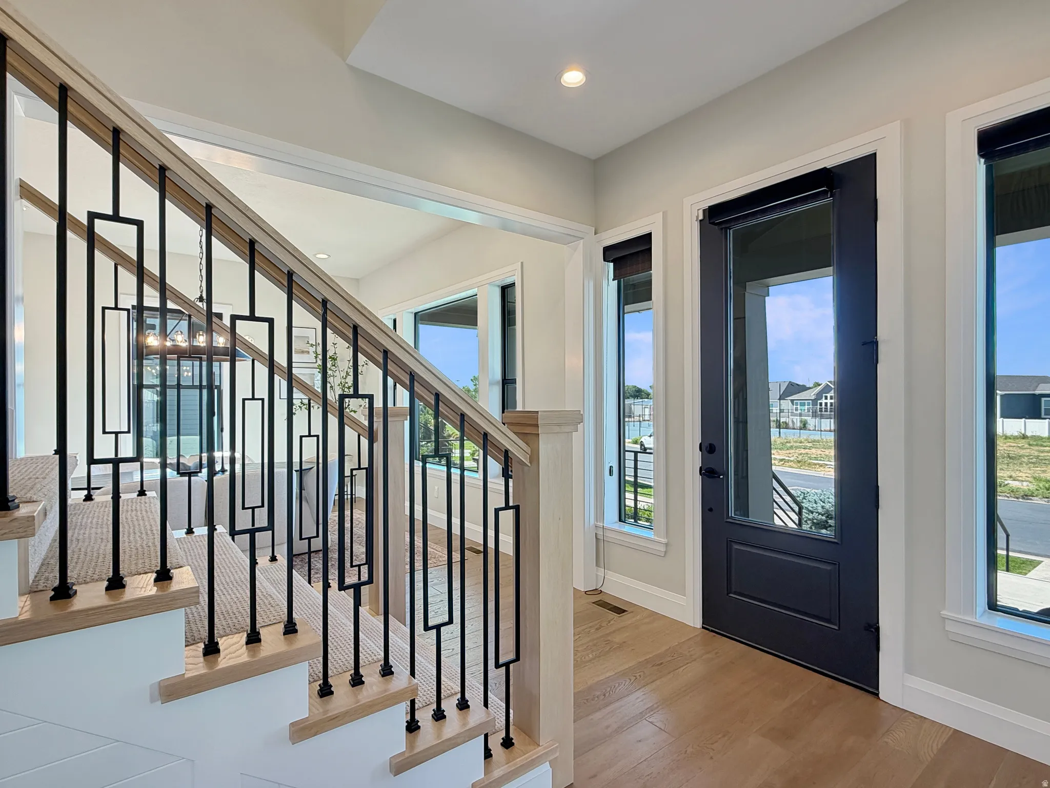 Hardwood flooring, contemporary black metal balusters, light wood handrail, recessed lighting, and a dark-framed glass paneled door