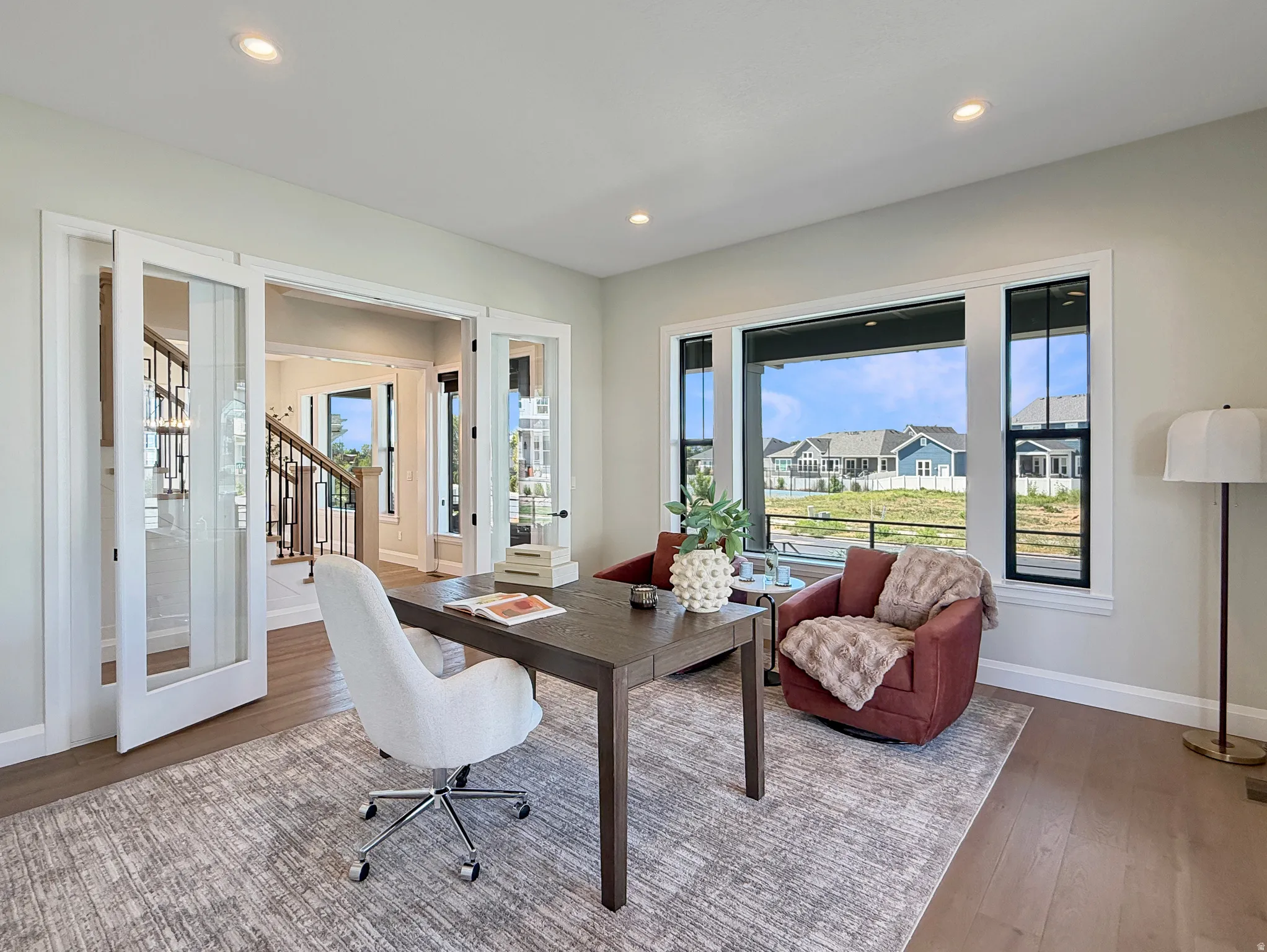 French doors with glass panels, recessed ceiling lighting, large windows with dark trim, light wood-finish flooring, and neutral wall tones