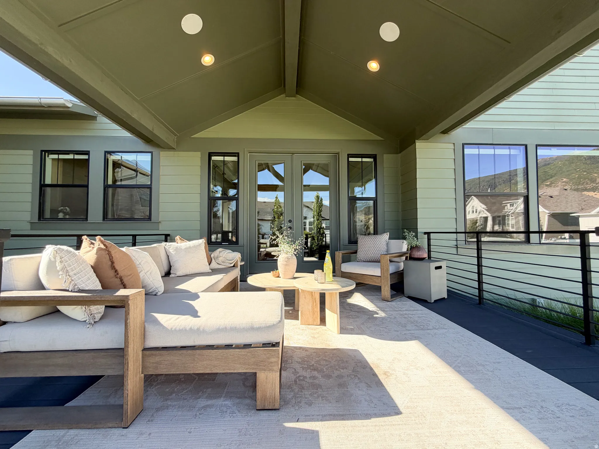 Covered patio with recessed lighting, double glass-paneled doors, multiple windows, and a black metal railing