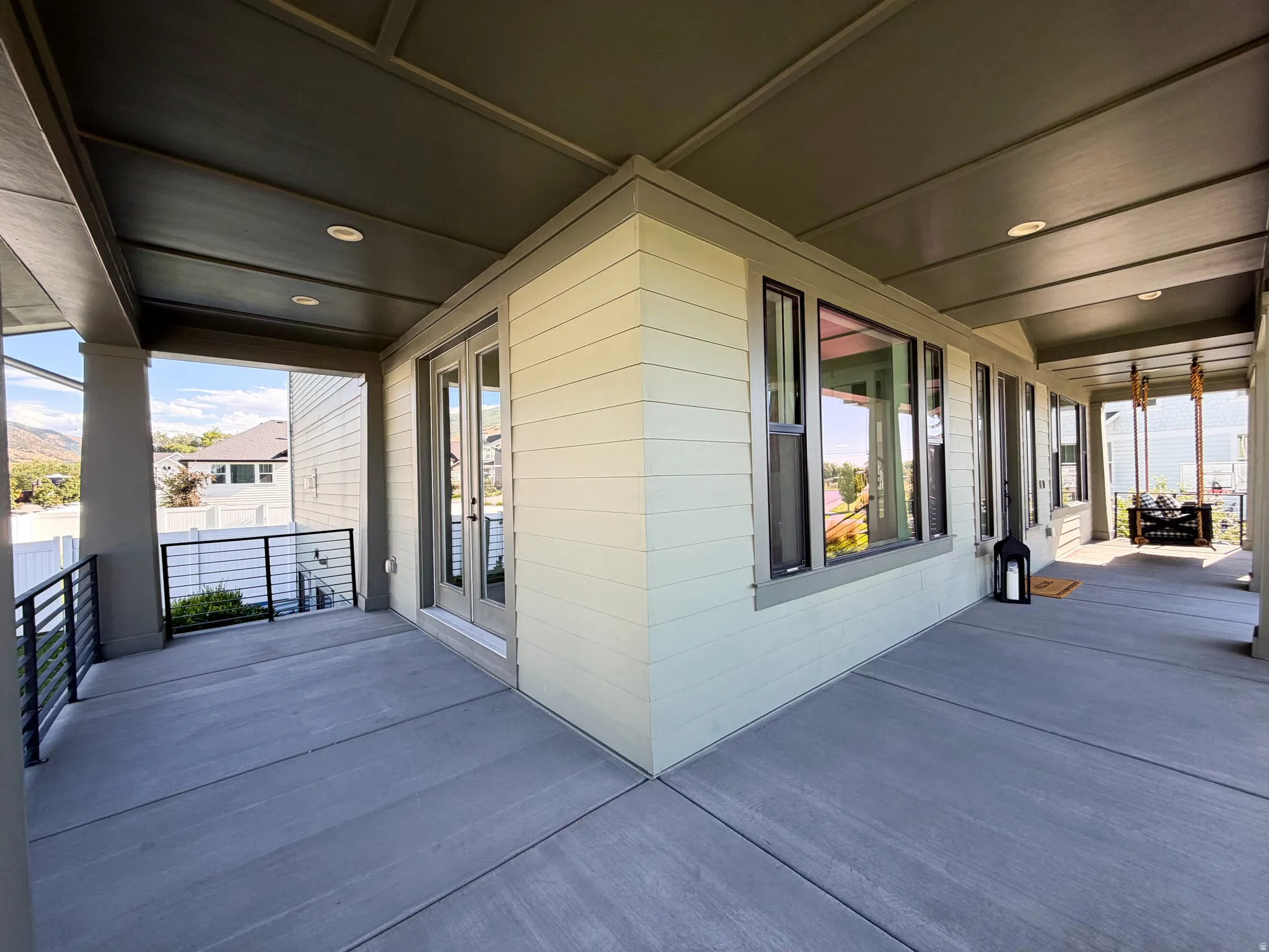 Covered concrete patio with recessed lighting, multiple windows, and a black horizontal bar railing
