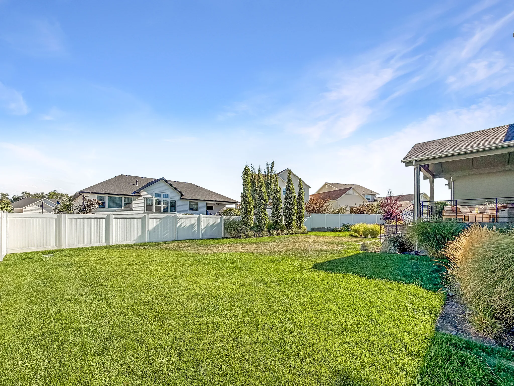Expansive backyard featuring a manicured lawn, established landscaping, and a white vinyl privacy fence