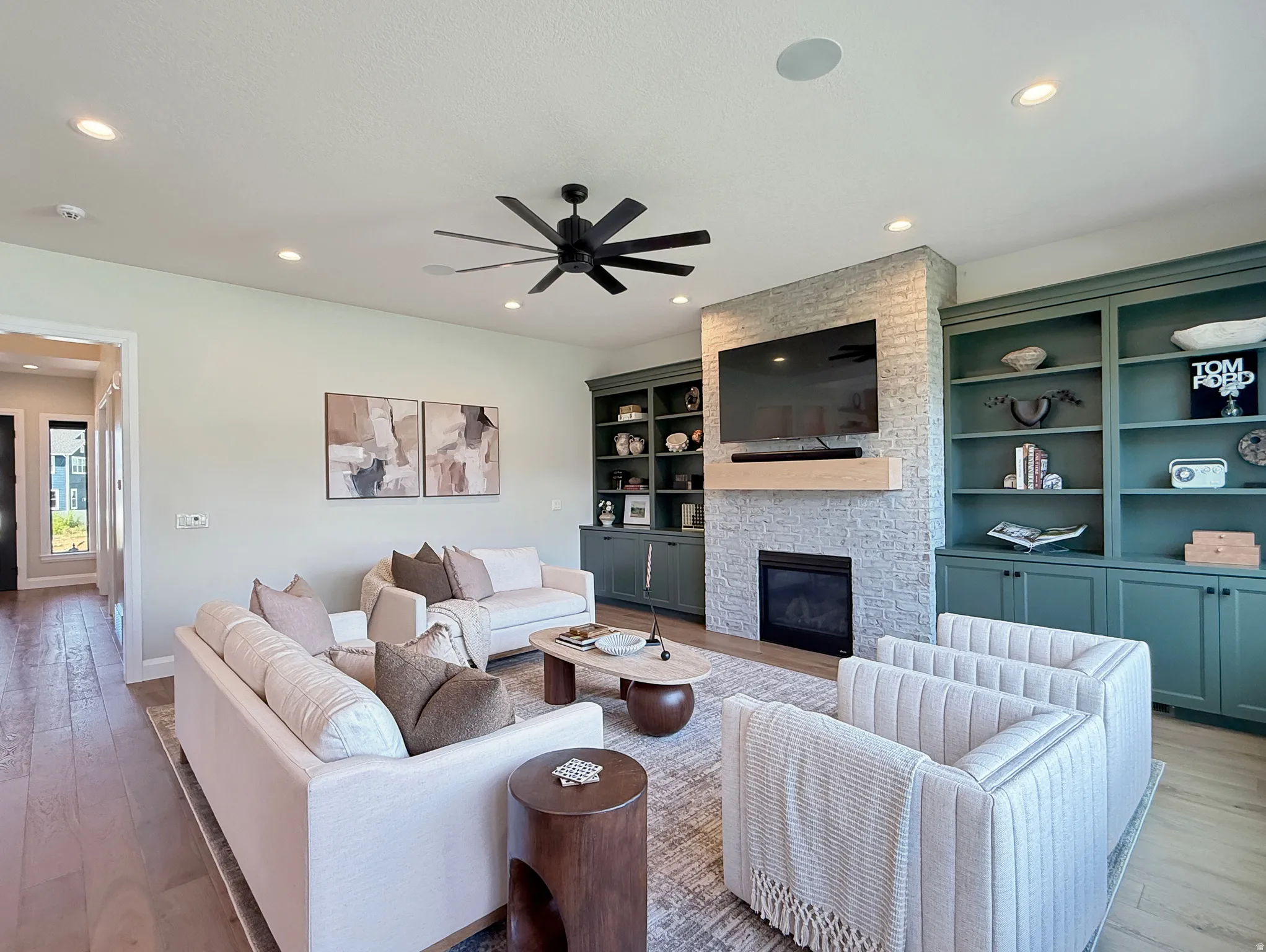 Recessed lighting, wood-finish flooring, ceiling fan, fireplace with light gray brick surround, and built-in shelving