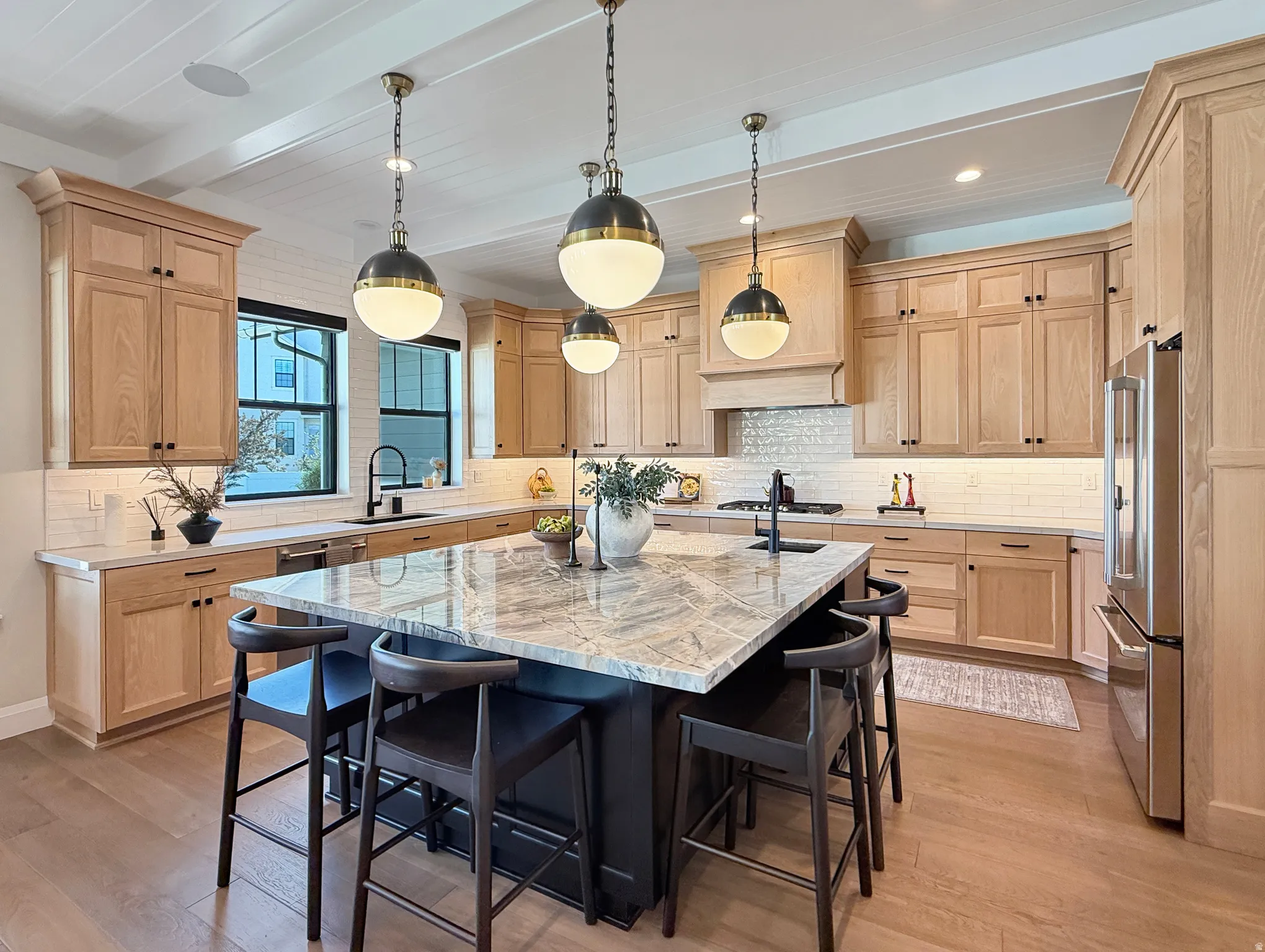 Expansive kitchen featuring light wood cabinetry, a large center island with a stone countertop, a tile backsplash, and wood-finish flooring