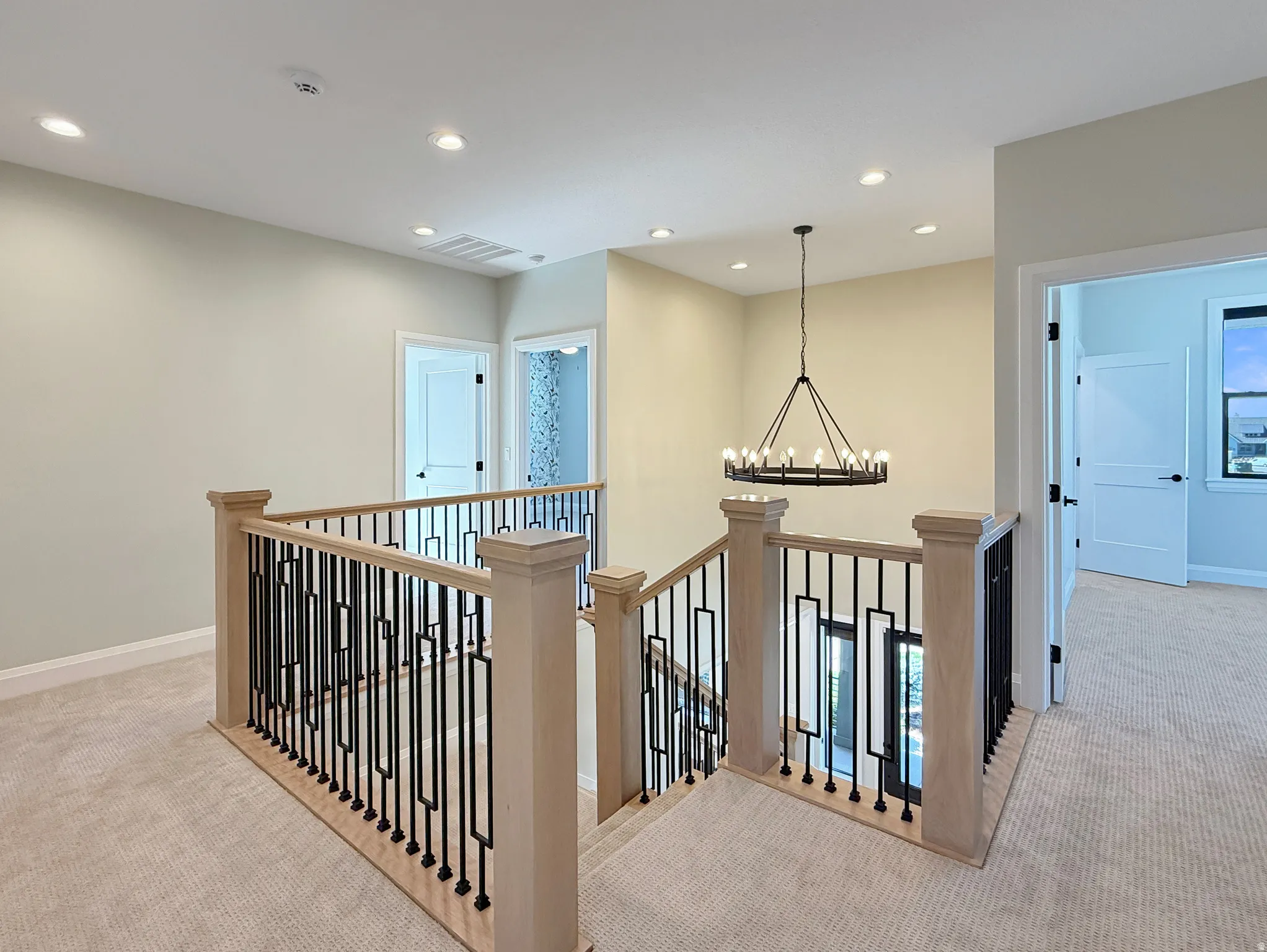 Staircase with light wood-finish handrails, contemporary black metal balusters, and recessed lighting