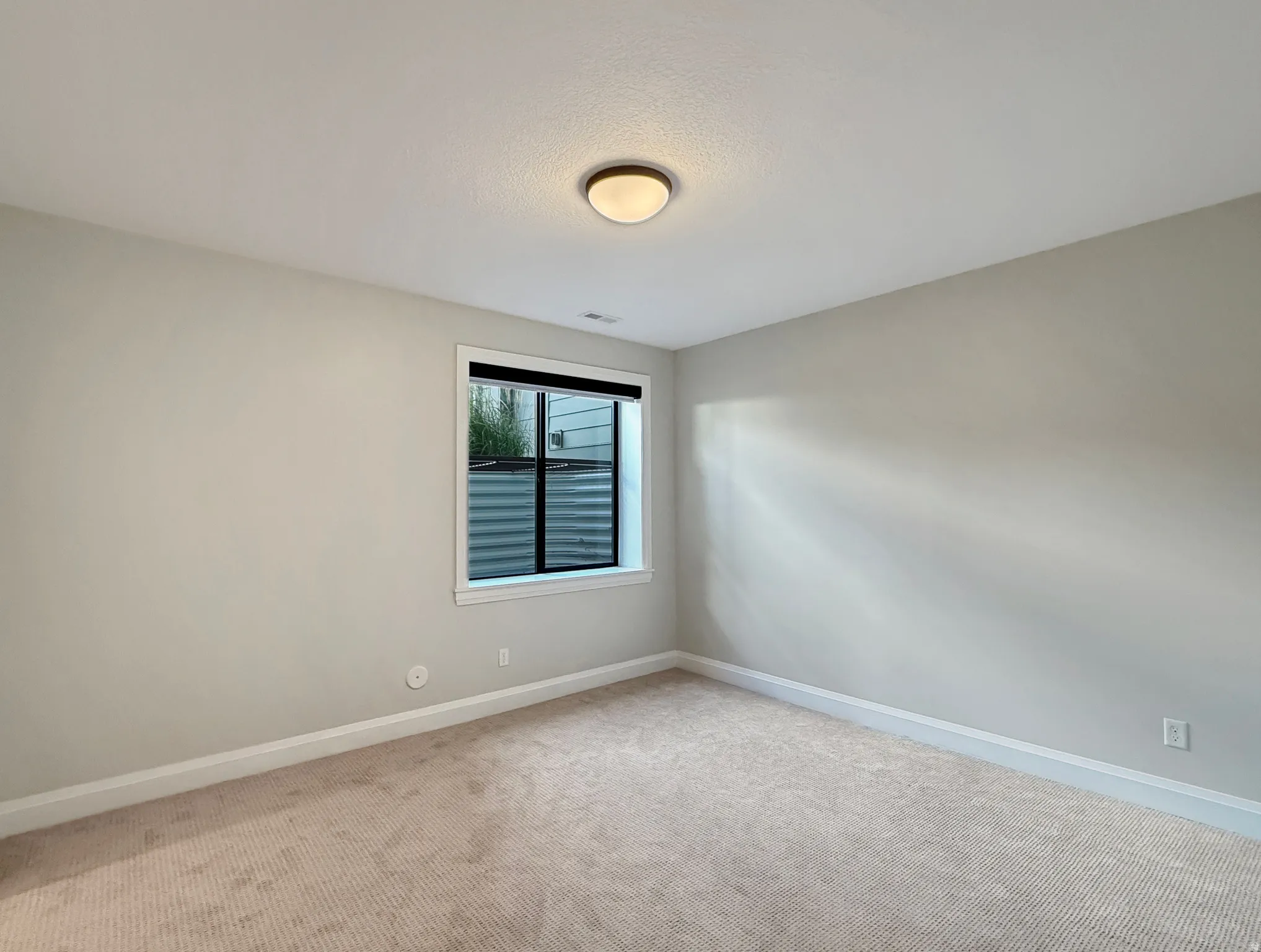 Carpeted flooring with light-colored walls, a single window, and a flush-mount ceiling light fixture