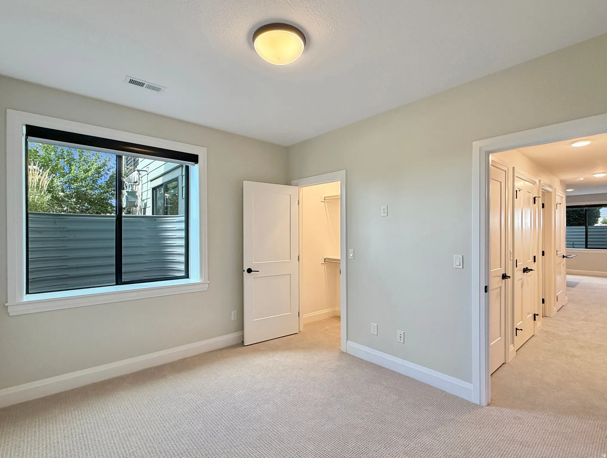 Neutral carpet flooring, recessed ceiling light, white trim, flat panel interior doors, and a window with blinds