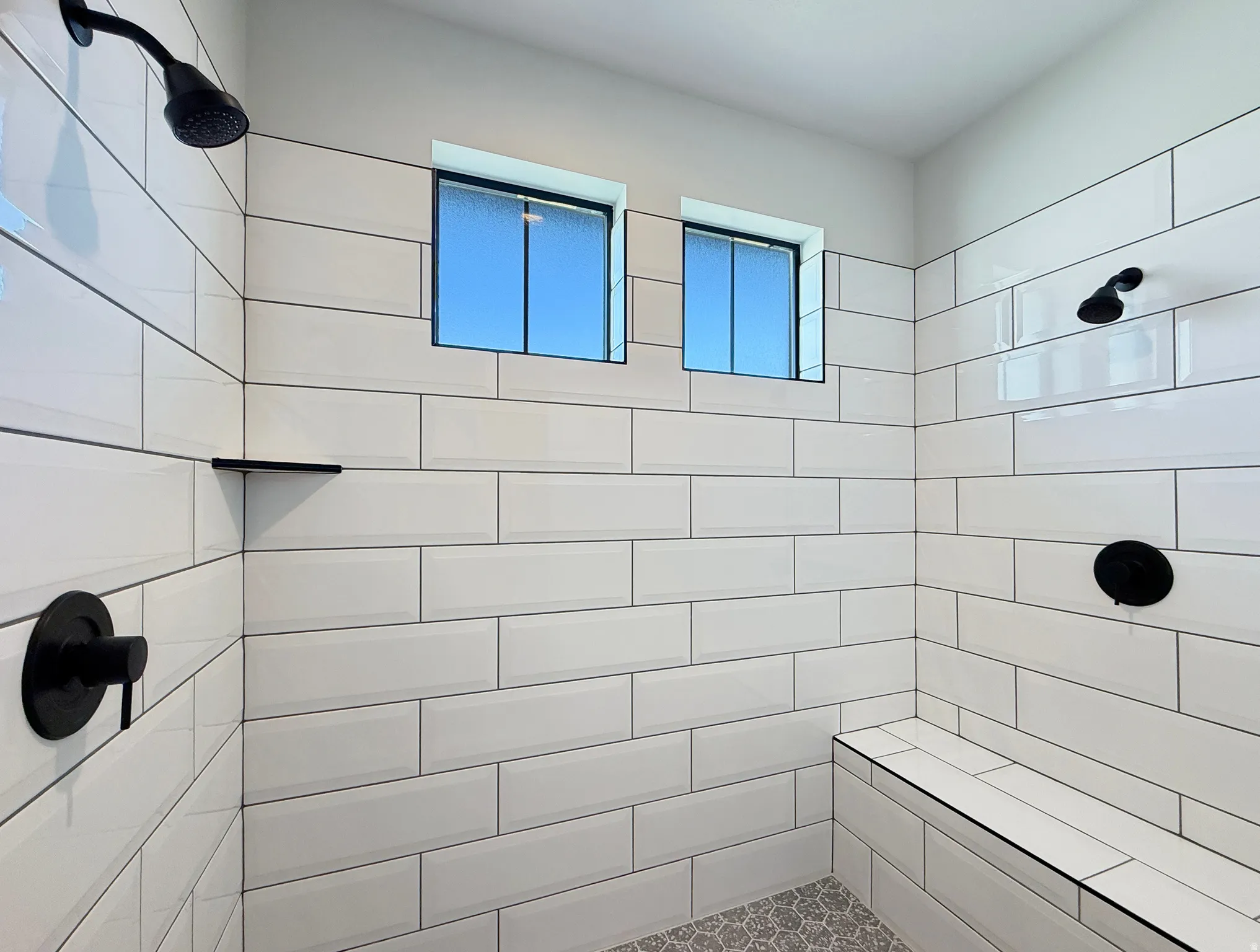 Shower with subway tile, built-in bench, two shower heads, and matte black fixtures