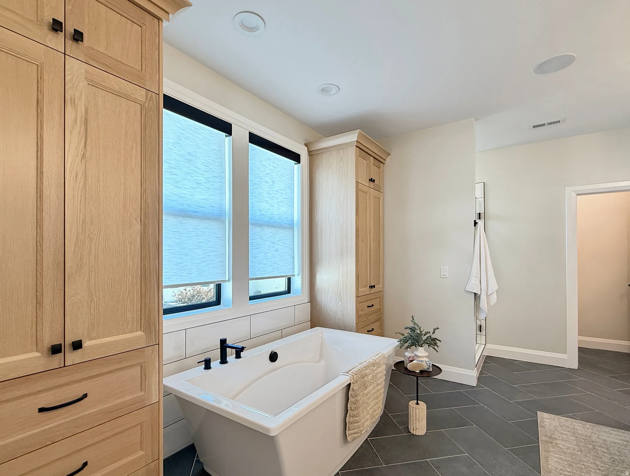 Freestanding soaking tub with a matte black faucet, surrounded by natural wood-finish cabinetry