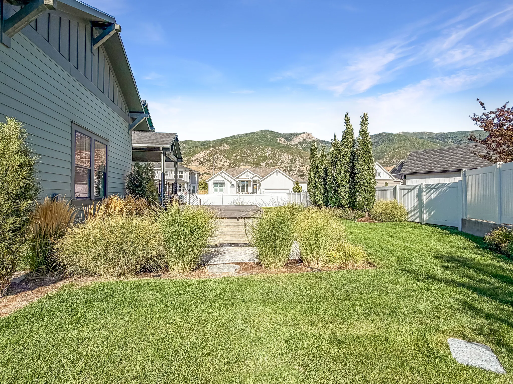 Backyard featuring a manicured lawn, established landscaping, and a white vinyl fence