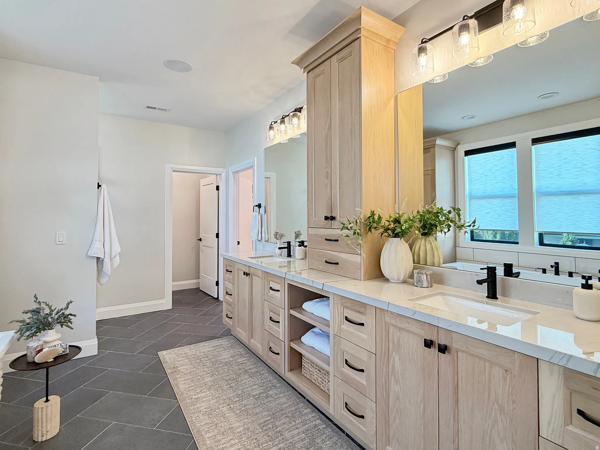 Dual vanity with light wood-finish cabinetry, integrated sinks, and matte black fixtures