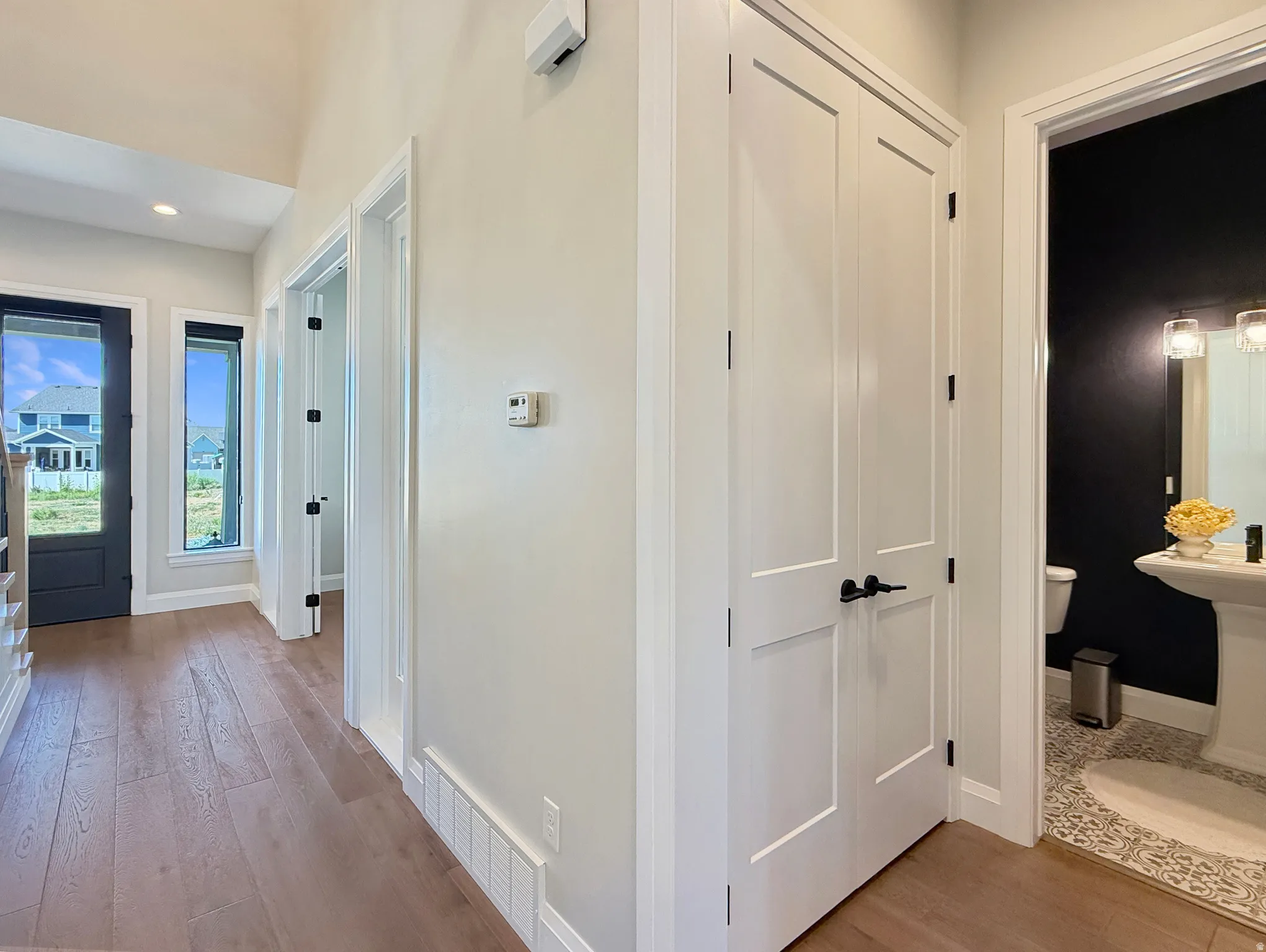 Wood-finish flooring, white paneled doors with black hardware, and a high vaulted ceiling