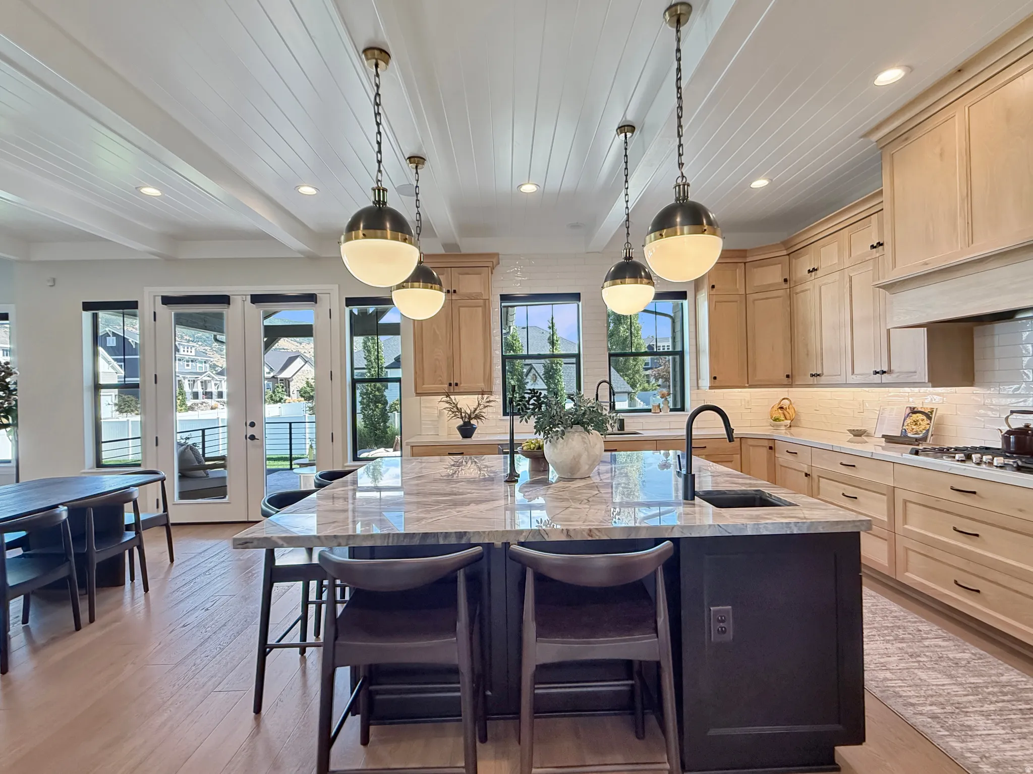 Kitchen featuring light wood cabinetry, a large kitchen island with a stone countertop, a built-in sink, and pendant lighting