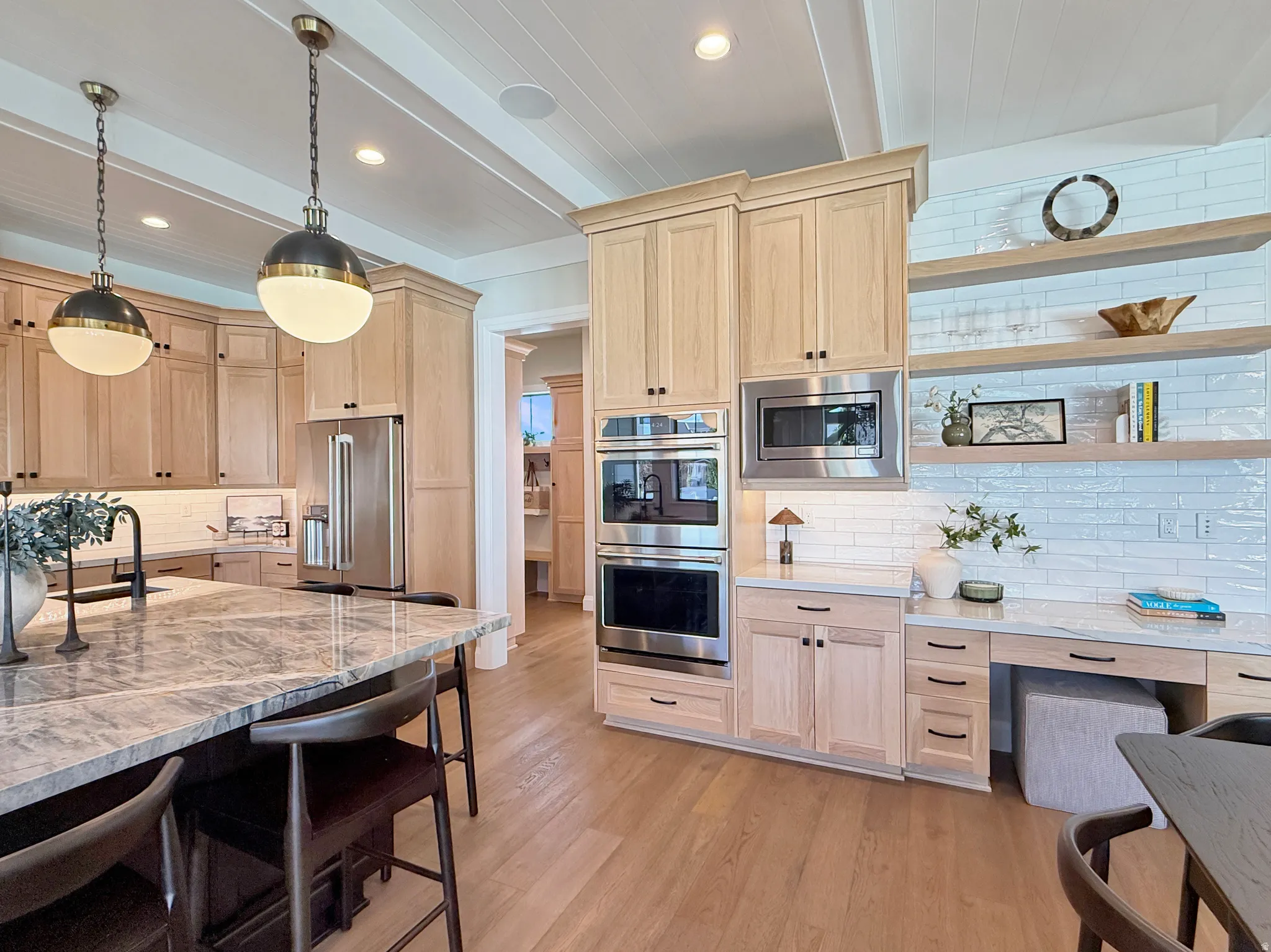 Light wood-finish cabinetry, stainless steel appliances, marble-finish countertops, wood-finish flooring, and a white subway tile backsplash