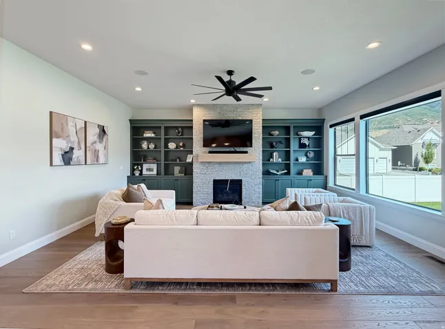 Living area featuring wood-finish flooring, built-in shelving, a stone fireplace, recessed lighting, and large windows