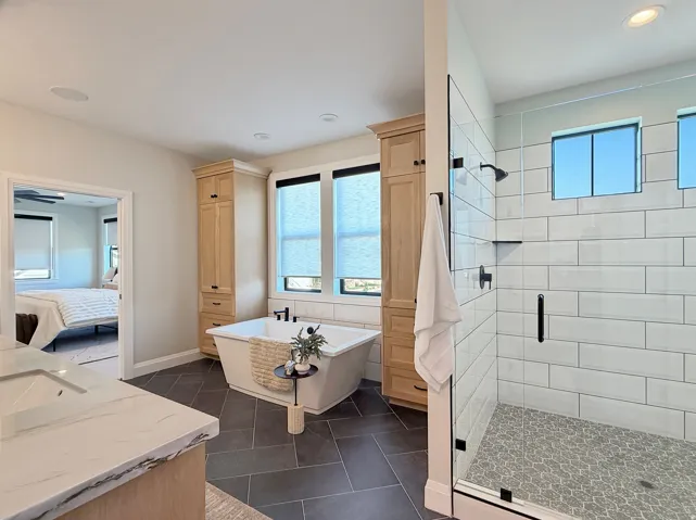 Freestanding soaking tub, floor-to-ceiling cabinetry, glass-enclosed shower with subway tile surround, patterned shower flooring, and dual rectangular windows