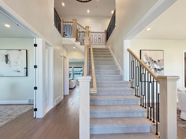 Two-story foyer with wood-finish flooring, carpeted staircase, and contemporary railing