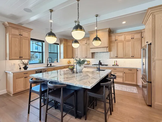 Expansive kitchen featuring light wood cabinetry, a large center island with a stone countertop, a tile backsplash, and wood-finish flooring