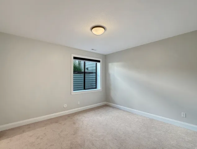 Carpeted flooring with light-colored walls, a single window, and a flush-mount ceiling light fixture