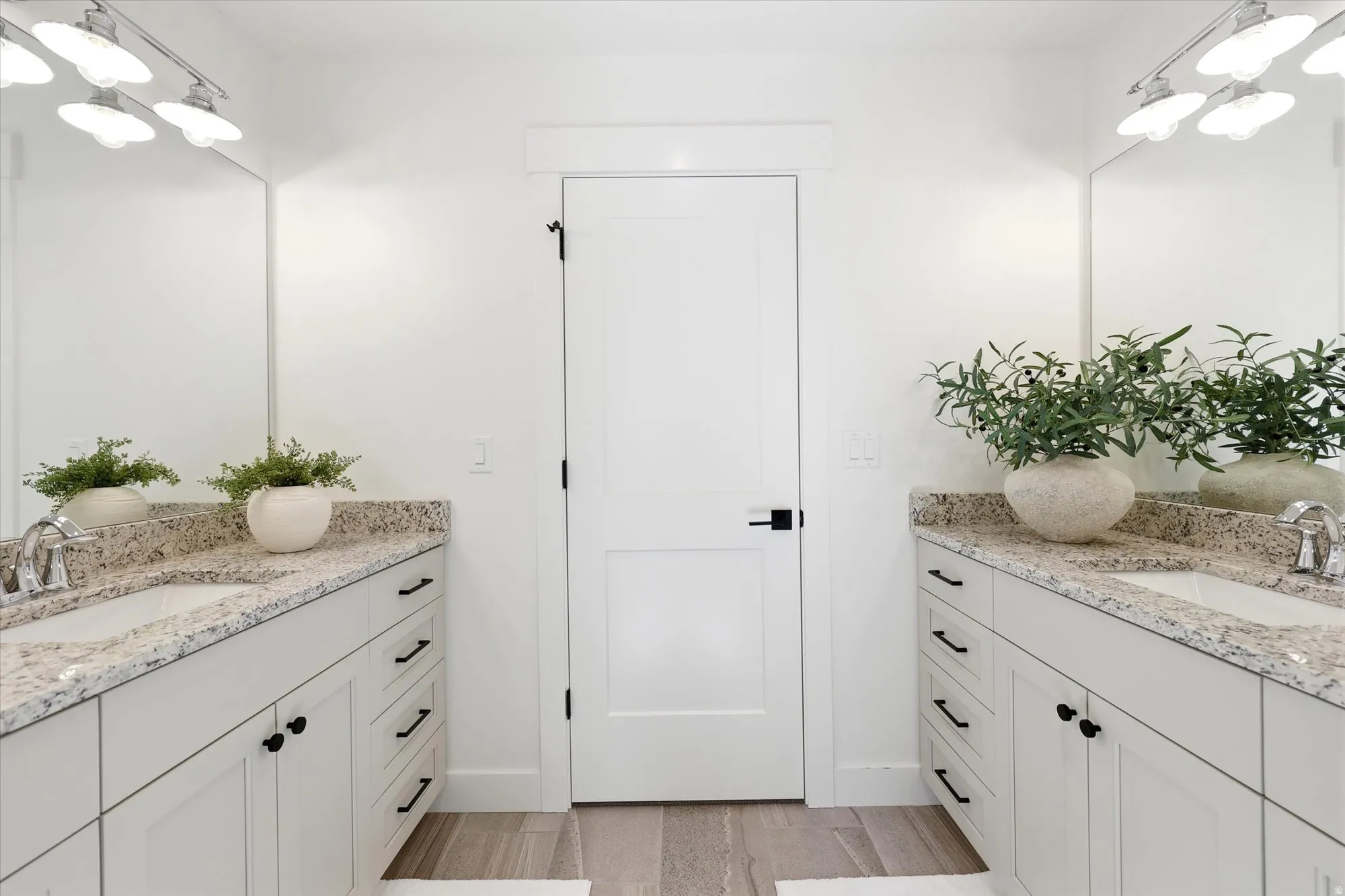 Dual vanity with light-toned countertops, integrated sinks, white cabinetry, and matte black hardware