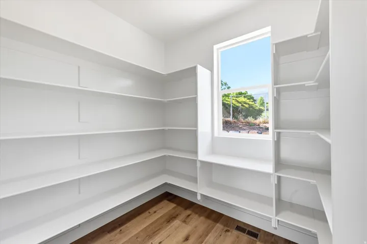 Spacious pantry featuring extensive built-in shelving, a large window, and wood-finish flooring