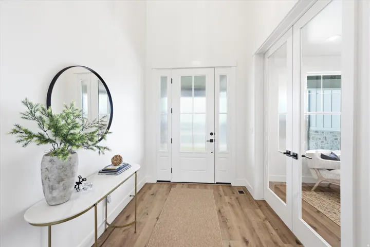Vaulted entryway with wood-finish flooring, white walls, and a front door with frosted glass panels