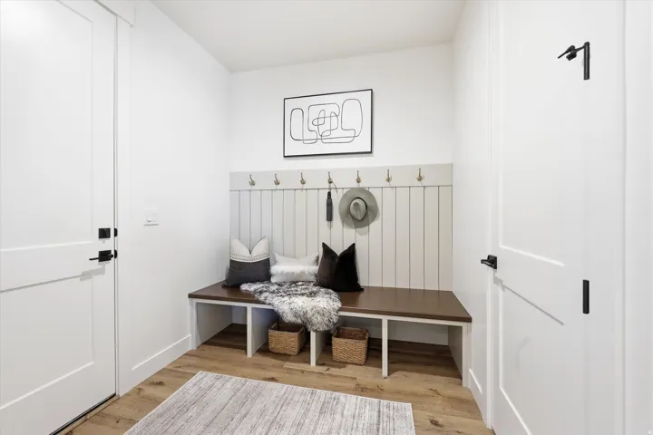 Wood-finish flooring, built-in bench with hooks, white paneled wall accent, modern flat-panel doors, and matte black door hardware