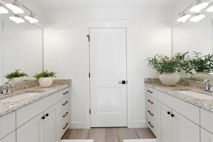 Dual vanity with light-toned countertops, integrated sinks, white cabinetry, and matte black hardware