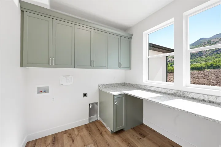 Sage green cabinetry with silver hardware, light-toned stone-finish countertop, wood-finish flooring, and white window frames