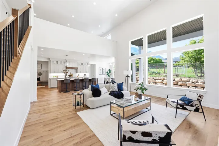 Two-story living area with high ceilings, expansive windows, wood-finish flooring, and a staircase with black metal balusters