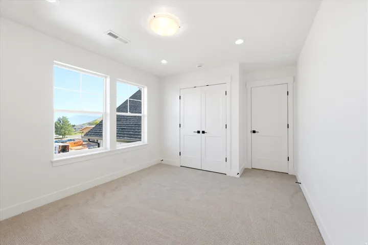 Bright, light-filled bedroom featuring expansive windows with natural illumination, neutral carpeting, and dual closets with white panel doors